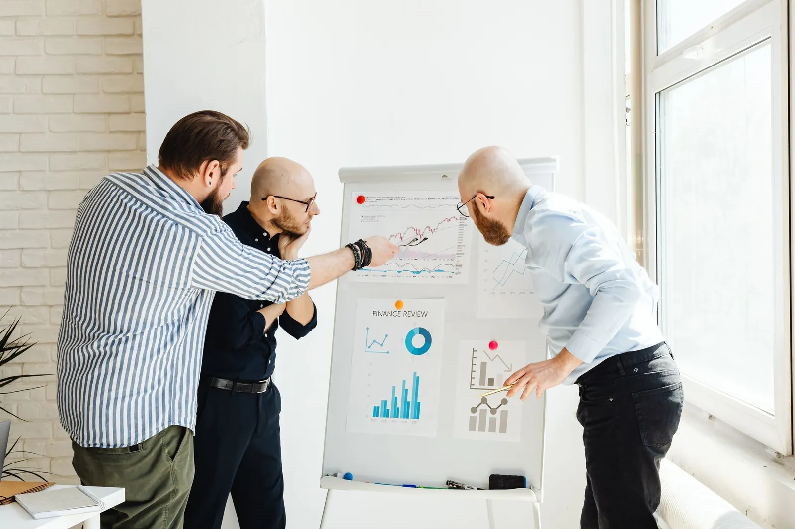 Three men pointing at graphs on a whiteboard